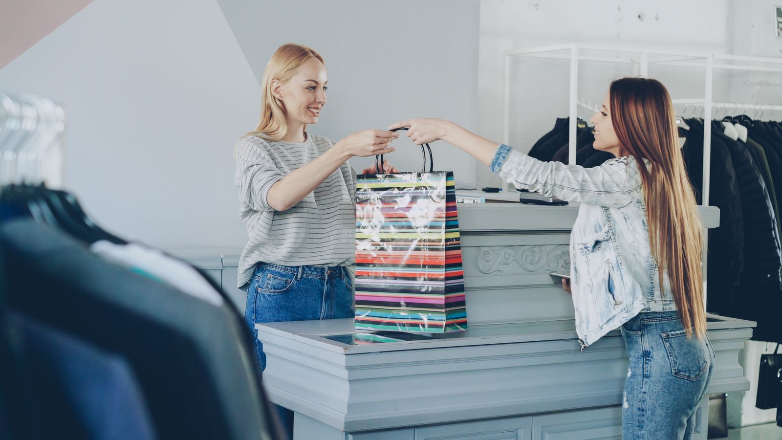 Eine Verkäuferin übergibt einer Kundin ihren Einkauf über die Ladentheke eines Bekleidungsgeschäfts.